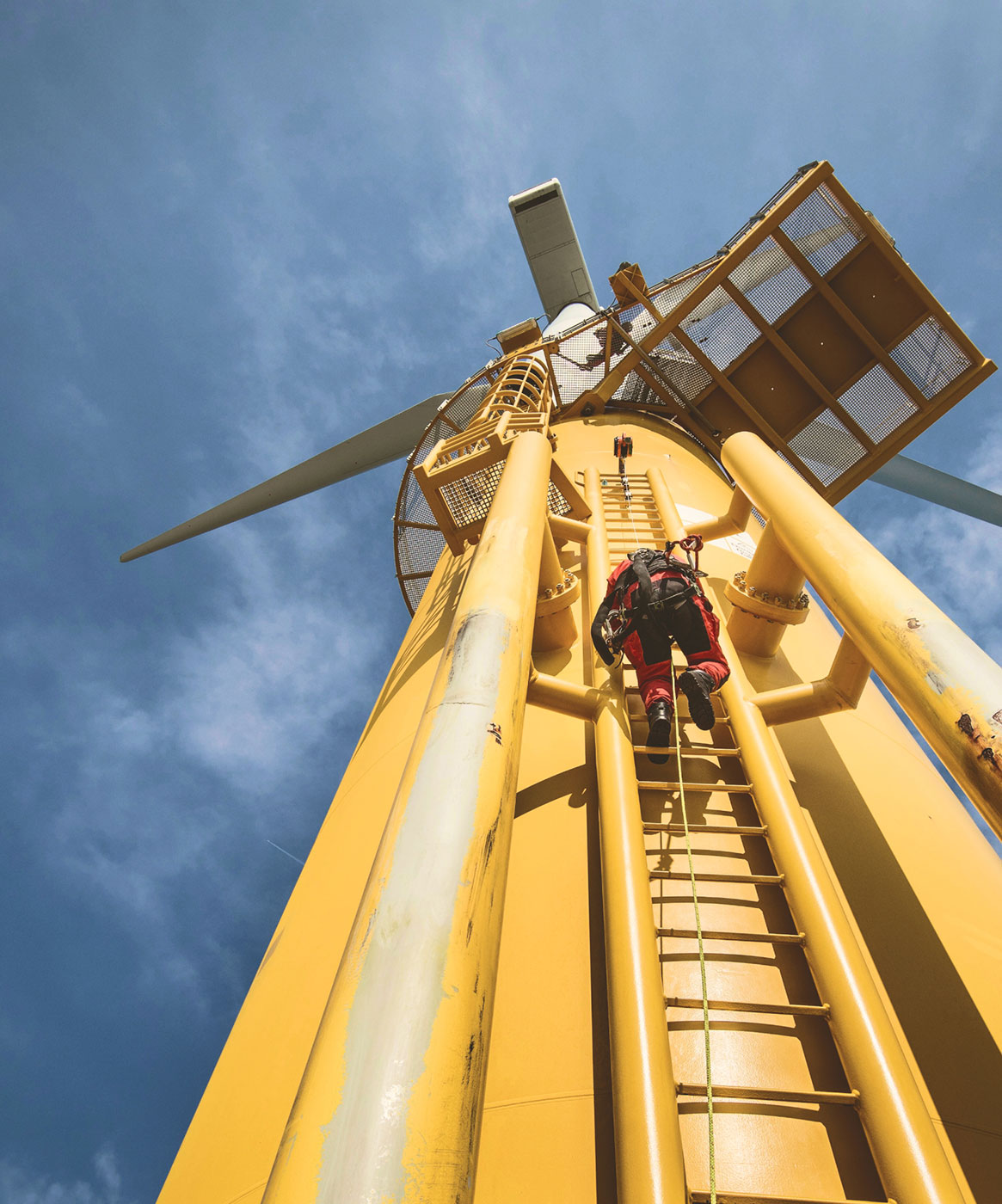 Maintenance worker climbing a yellow wind turbine against a dramatic cloudy sky