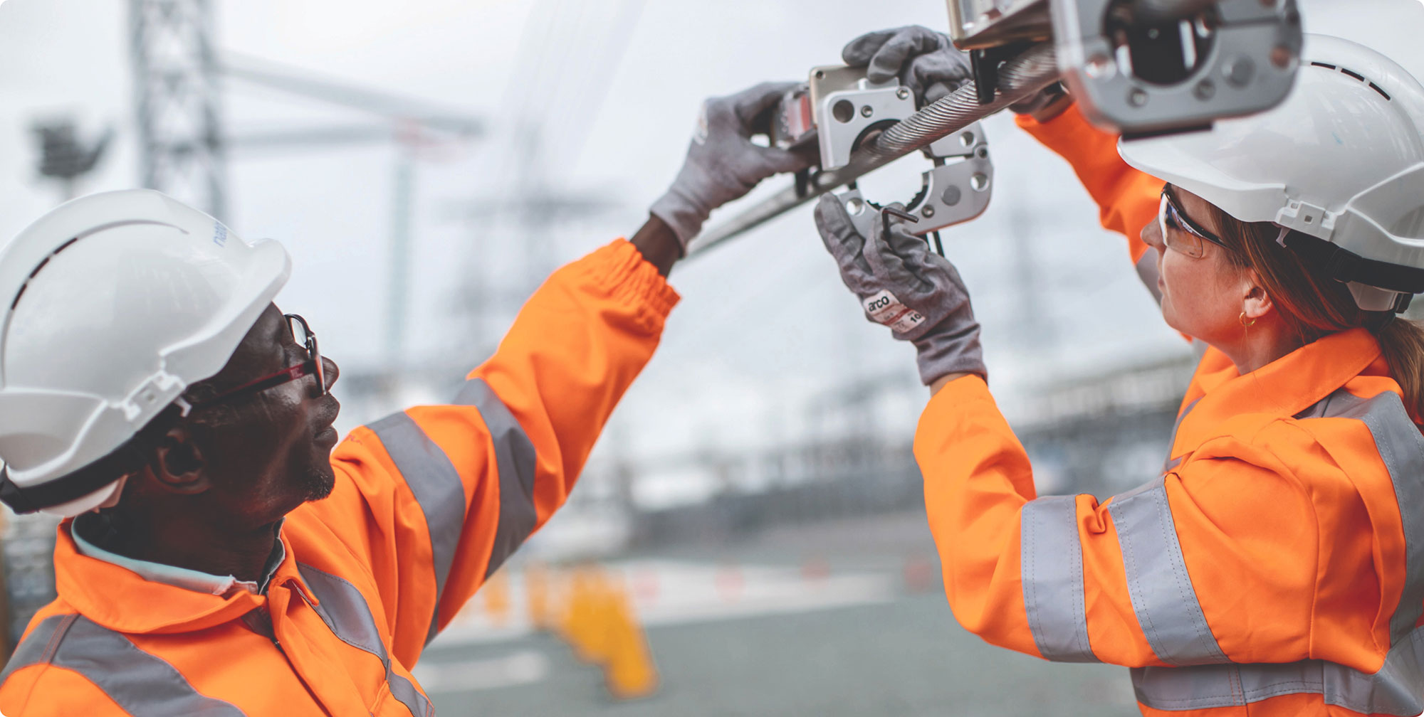 Two National Grid maintenance workers in orange safety gear collaborating on equipment maintenance